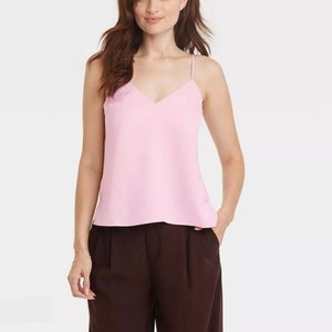 Könnte beinhalten: Ein pinkfarbenes, ärmelloses Oberteil mit V-Ausschnitt. Das Oberteil ist aus einem glatten, seidenartigen Stoff.