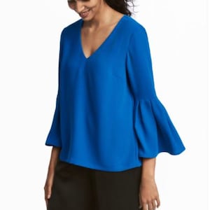 Puede incluir: Una blusa azul brillante con cuello en V y mangas largas acampanadas. La blusa está hecha de una tela suave y ligera.