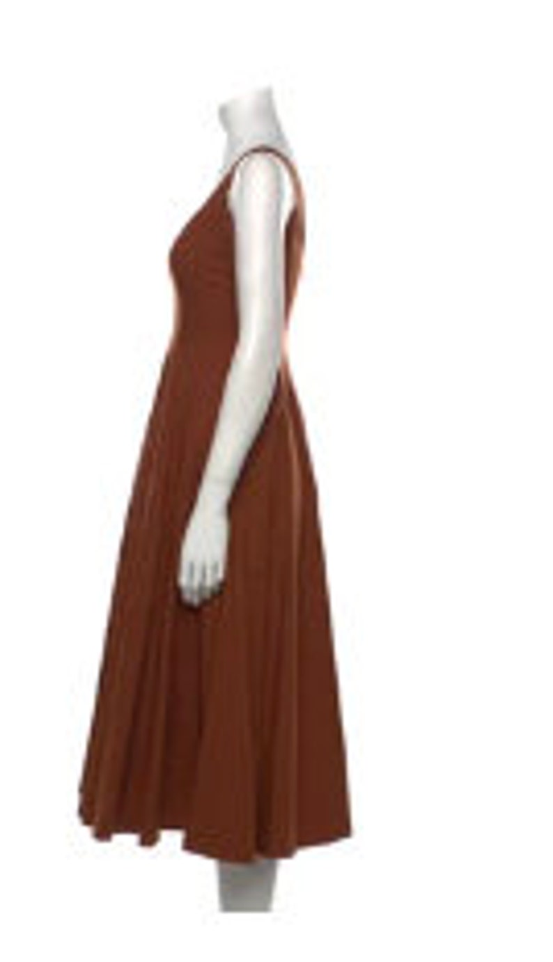 Puede incluir: Un vestido midi de color &oacute;xido con cuello redondo y tirantes finos. El vestido tiene un corpi&ntilde;o ajustado y una falda fluida.