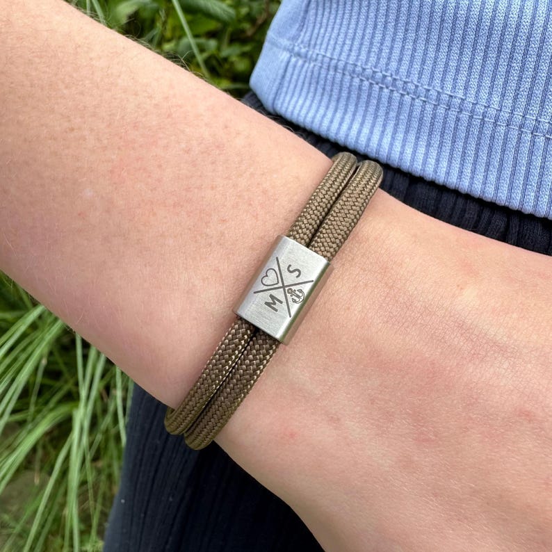 May include: A brown paracord bracelet with a silver metal clasp engraved with the letters "M & S" and a heart symbol.