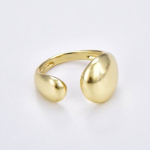 May include: A gold-toned ring with a large, smooth, oval-shaped band. The ring is open on one side, creating a unique and modern design.
