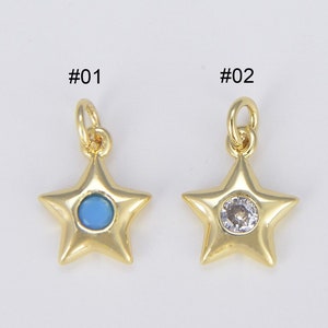 May include: Two gold star-shaped charms with different center stones. The charm on the left has a blue stone, and the charm on the right has a clear stone. Both charms have a loop at the top for attaching to a necklace or bracelet.