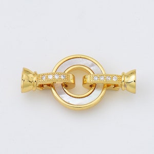 May include: Gold-tone metal clasp with a white mother-of-pearl centre and clear crystal accents.