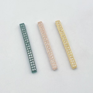 May include: Three bar-shaped jewelry connectors with clear rhinestones. The connectors are gold, rose gold, and dark green.