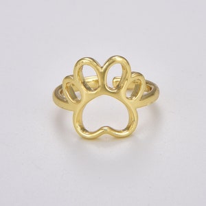May include: A gold-colored ring featuring a paw print design. The ring's paw print is open, with the outline of the paw forming the ring's main design element. The ring is likely made of metal and is set against a white background.