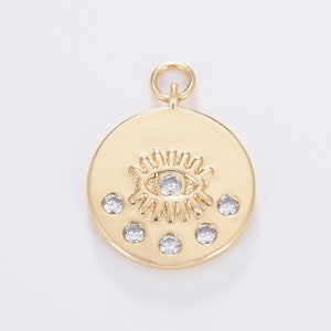 May include: Gold-toned charm with a detailed eye design and four smaller clear rhinestones around it. The charm is round and has a loop at the top for attaching to a necklace or bracelet.