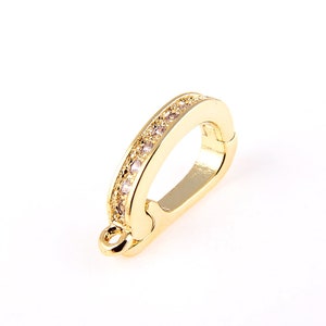 Könnte beinhalten: Vergoldeter Metallverschluss mit einer Reihe von klaren Strasssteinen. Der Verschluss ist so konzipiert, dass er als Verbindungselement für Schmuck verwendet werden kann.