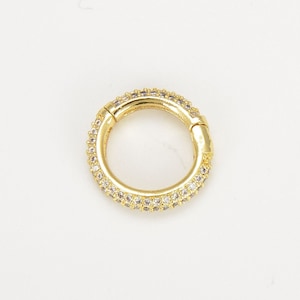 May include: A gold hoop earring with a row of clear cubic zirconia stones around the edge.