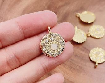 May include: Gold-toned pendant charms with a circular design featuring a white stone and clear rhinestones. The charms have a loop at the top for attaching to jewelry.