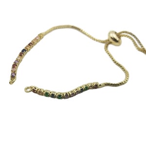 May include: A gold adjustable bracelet with a chain and a row of colorful gemstones.