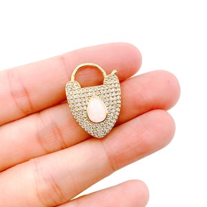 May include: Gold padlock charm with a clear teardrop-shaped stone set in the center, surrounded by clear cubic zirconia stones.