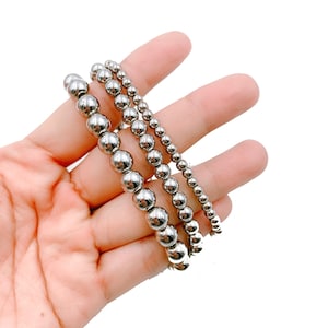 May include: Three silver beaded bracelets of varying sizes, stacked on top of each other.