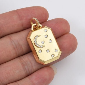 May include: Gold pendant necklace charm with a crescent moon and stars design. The charm is rectangular with a beveled edge and is set with clear cubic zirconia stones.