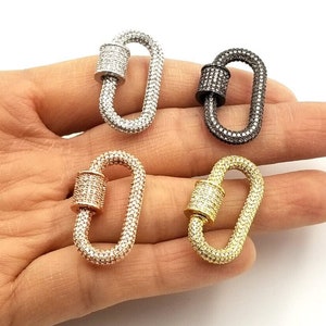 May include: Four oval-shaped lobster clasps with a pave setting of clear rhinestones. The clasps are in four different metal finishes: silver, gold, rose gold, and black.