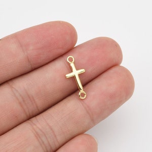 May include: A gold-colored cross charm with a simple design. The charm has a small loop at the top and bottom for attaching to jewelry. The cross is a religious symbol, often used in necklaces, bracelets, and earrings.