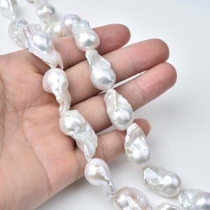 May include: A strand of large, irregular white baroque pearls. The pearls have a lustrous, iridescent sheen and vary in size and shape. The pearls are strung together, creating a necklace or bracelet.