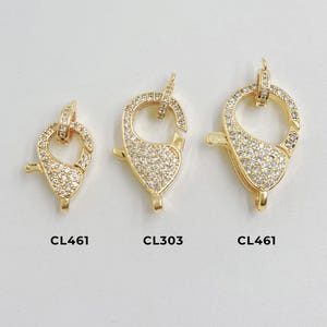 May include: Three gold-coloured jewellery clasps with clear crystal accents. The clasps are in different sizes and shapes, with a teardrop-like design. The clasps are labelled with the text "CL461" and "CL303".