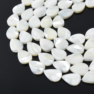 May include: Close-up of a collection of pearlescent white teardrop-shaped beads. The beads have a smooth, glossy surface and are arranged closely together. The background is a solid black.