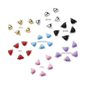 May include: Assortment of magnetic heart clasps in various colors, including gold, silver, black, light blue, light purple, and pink. Each clasp is made of metal and features a heart shape.