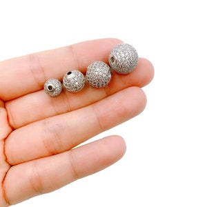 May include: Four silver round beads with a clear crystal-like finish. The beads are different sizes and are arranged in a row from smallest to largest.