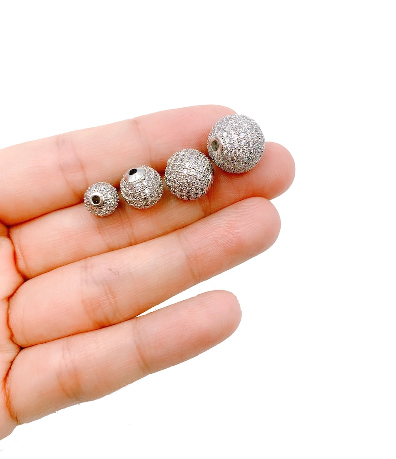 May include: Four silver round beads with a clear crystal-like finish. The beads are different sizes and are arranged in a row from smallest to largest.