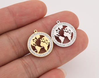 May include: Two round pendants featuring a world map design. One pendant is gold-toned, the other is silver-toned. Both have a border of clear crystals. Each pendant has a small loop at the top for attaching to a chain or other jewelry.
