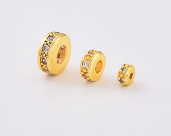 May include: Three gold-colored spacer beads with clear, sparkling accents. The beads are in graduated sizes, with the largest bead on the left and the smallest on the right. The beads have a circular shape with a hole in the center.