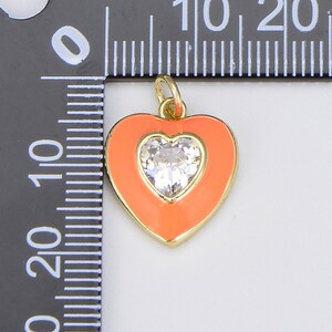 May include: A gold heart-shaped charm with a clear rhinestone in the center. The heart is surrounded by a bright orange enamel.