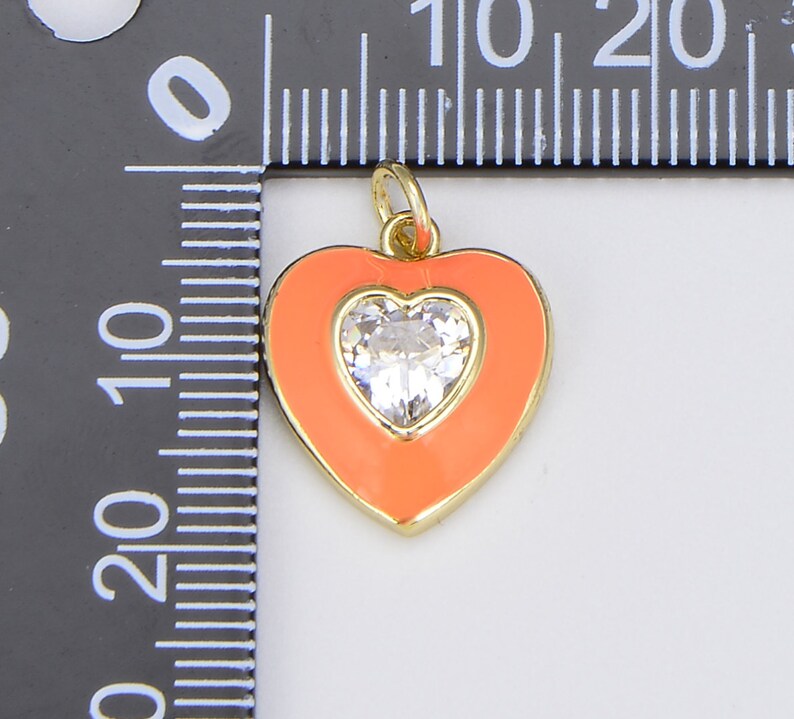 May include: A gold heart-shaped charm with a clear rhinestone in the center. The heart is surrounded by a bright orange enamel.