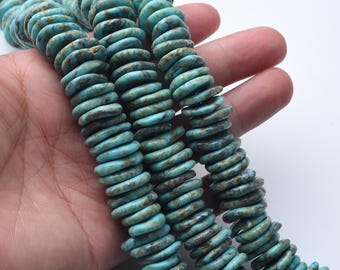 May include: Strands of turquoise-colored, disc-shaped beads. The beads have a distressed, mottled appearance with darker brown and black accents. The beads are strung together, creating a necklace or bracelet component. The beads are approximately 0.5 inches in diameter.