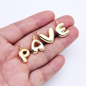 Könnte beinhalten: Goldfarbene Metall-Buchstabenanhänger in Form der Buchstaben P, A, V und E. Die Anhänger sind leicht gepolstert und haben oben ein Loch zum Anbringen an einer Kette oder einem Armband.