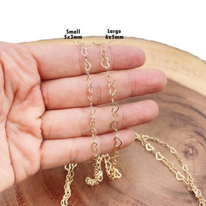 May include: Two gold heart-shaped chains, one small and one large, are shown on a hand. The small chain is 5x3mm and the large chain is 6x5mm.