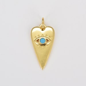 Puede incluir: Colgante de corazón dorado con un amuleto de ojo turco azul. El colgante es un símbolo popular de protección y buena suerte.