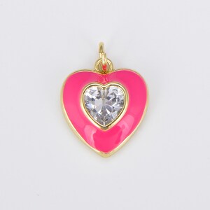 May include: A pink enamel heart charm with a clear rhinestone in the center. The charm is gold-toned and has a loop at the top for attaching to a necklace or bracelet.