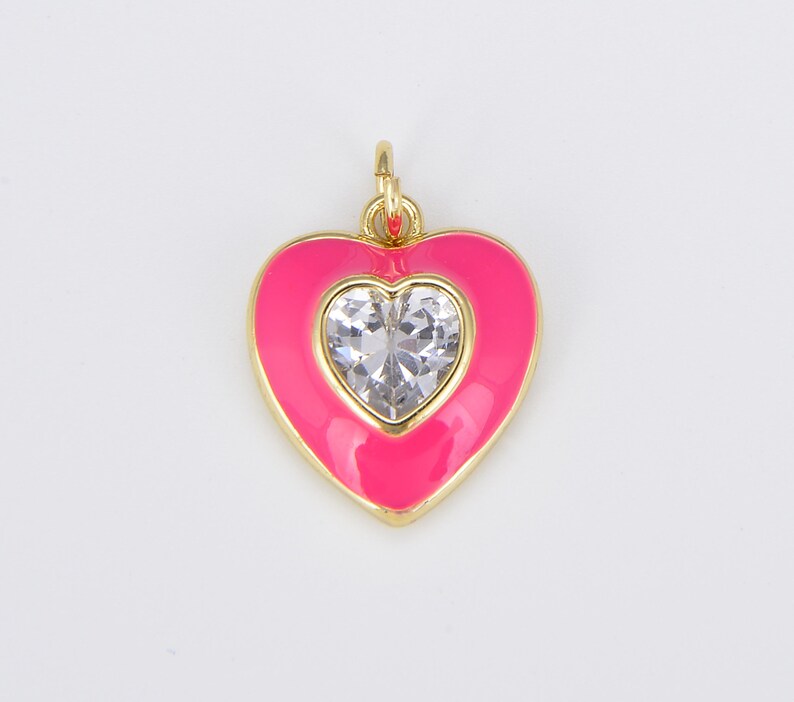 May include: A pink enamel heart charm with a clear rhinestone in the center. The charm is gold-toned and has a loop at the top for attaching to a necklace or bracelet.