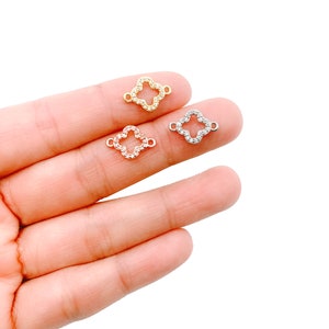 May include: Three clover-shaped jewelry connectors in gold, rose gold, and silver. Each connector is encrusted with small, clear crystals. The connectors have small loops on each side for attaching to other jewelry components.