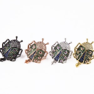 May include: Four beetle charms with green, blue, and red accents. The beetles are made of metal and have a shiny finish. The charms are available in black, rose gold, silver, and gold.