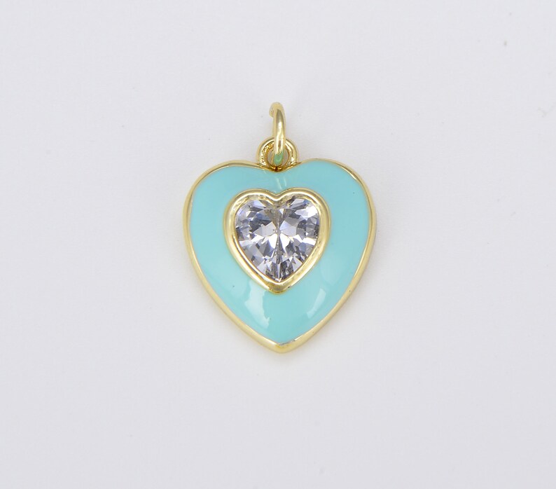 May include: A gold heart-shaped charm with a clear crystal in the center. The heart is outlined in gold and has a light blue enamel finish.