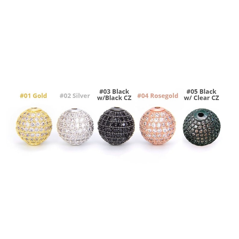 May include: Five round beads with clear or black cubic zirconia stones. The beads are gold, silver, black, rose gold, and black with clear stones.