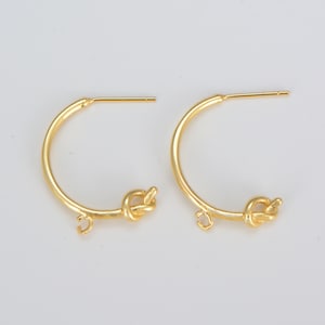 May include: A pair of gold-colored hoop earrings. Each earring features a half-circle design with a knot detail at the bottom and a post for piercing. The earrings are displayed against a white background.