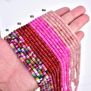 May include: A hand displays strands of small, colorful beads. The strands are numbered 01 through 04, showcasing a variety of colors including green, red, pink, and light pink. The beads appear to be uniform in size and shape.