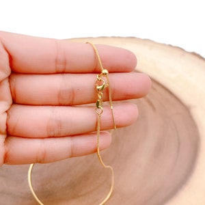 May include: A gold chain necklace with a sliding clasp and a small ball at the end of the slider. The chain is thin and delicate.