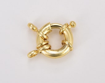 Könnte beinhalten: Ein goldfarbener, runder Federringverschluss. Der Verschluss hat ein kreisförmiges Design mit einer Scharnieröffnung und einem kleinen Hebel. Der Verschluss dient zum Sichern von Schmuckstücken. Der Verschluss besteht aus glänzendem Metall.