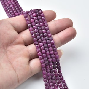 May include: Strands of faceted, square-cut ruby beads in varying shades of deep pink and red. The beads are strung together, showcasing their geometric shape and natural color variations. Ideal for jewelry making.