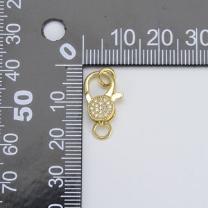 May include: Gold-tone lobster clasp with a round, clear crystal-encrusted accent. The clasp is approximately 1 cm in diameter.