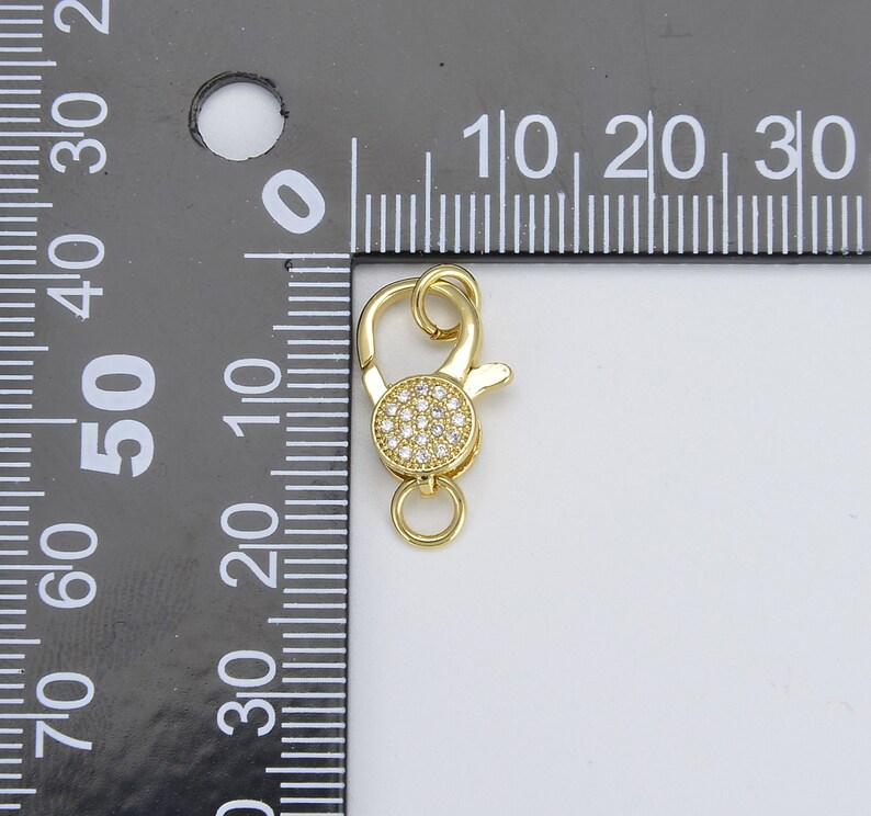 May include: Gold-tone lobster clasp with a round, clear crystal-encrusted accent. The clasp is approximately 1 cm in diameter.