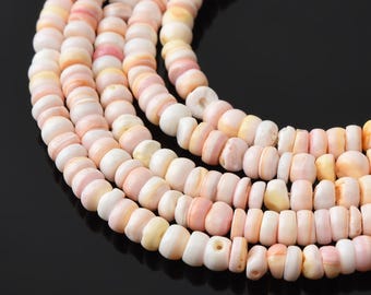Op de afbeelding: Close-up van verschillende strengen schelpkralen in pastelkleuren. De kralen zijn een mix van wit, roze en geel. De kralen zijn rond en licht afgeplat, geregen om een ketting of armband te creëren.
