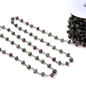Könnte beinhalten: Strang aus facettierten grünen und weinroten Edelsteinperlen, auf einer dunklen Metallkette aufgereiht. Die Perlen sind eine Mischung aus grünen und weinroten Farben. Eine Spule der gleichen Perlenkette ist sichtbar.