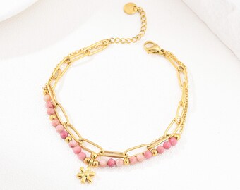 Könnte beinhalten: Ein goldenes Kettenarmband mit rosa Perlen und einem kleinen Blumenanhänger. Das Armband ist aus Edelstahl und hat einen Karabinerverschluss.