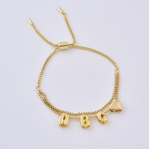 May include: Gold-colored adjustable bracelet featuring the letters "A", "B", and "C", along with a heart charm. The bracelet has a delicate chain design and a sliding clasp for adjustment. The letters and heart are in a rounded font.